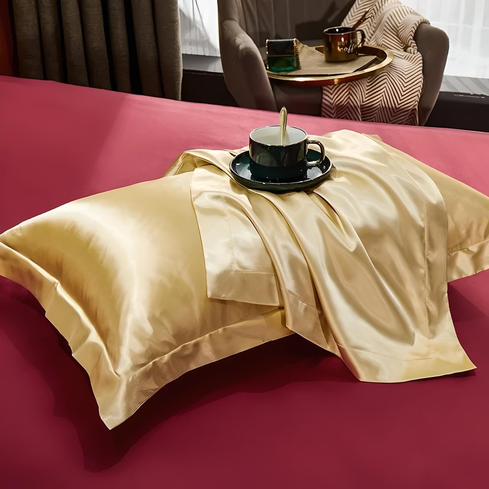 Luxurious gold silk pillowcase and matching sheet set on a red bed, featuring a black cup and saucer. Perfect for elegant bedroom decor.