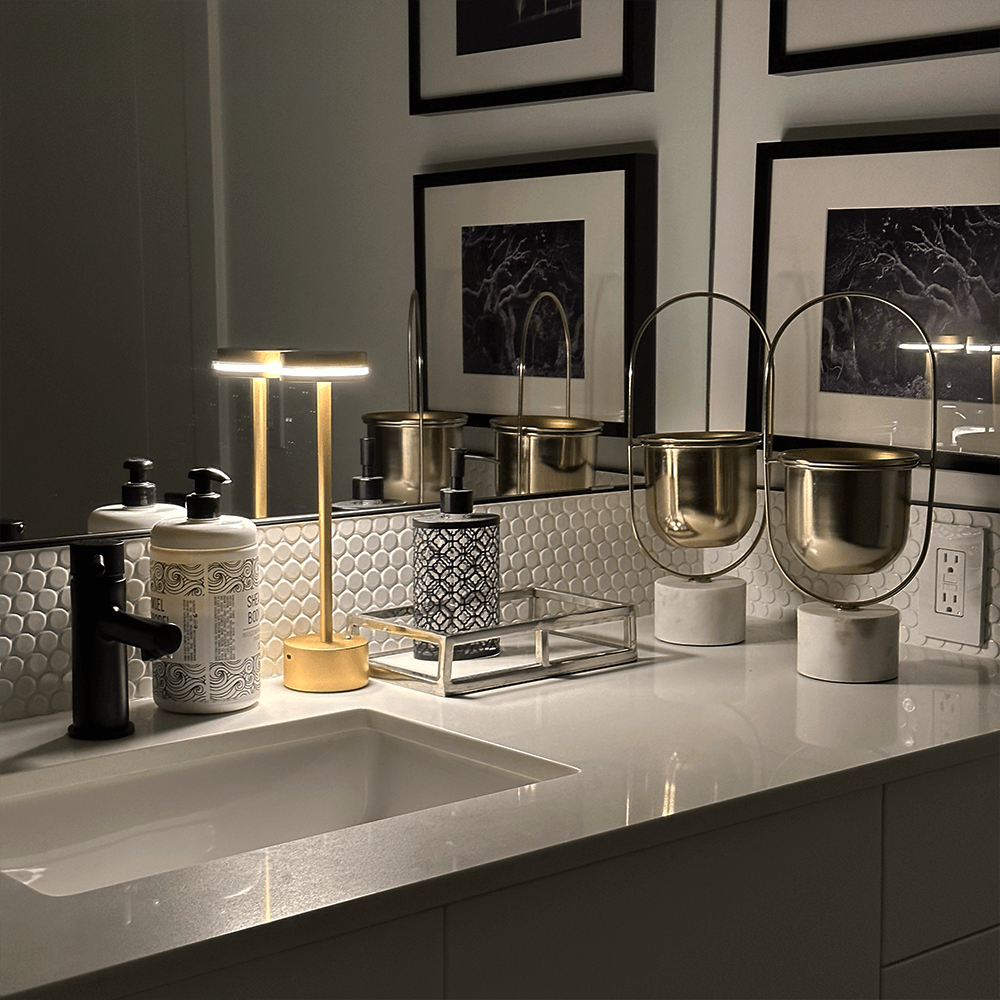 Modern bathroom vanity with elegant gold accents, featuring a sleek black faucet, decorative soap dispensers, and framed wall art. Luxurious interior design.