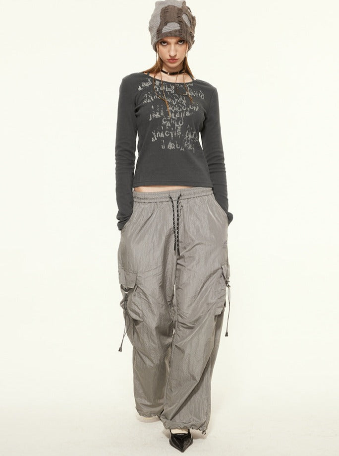 Woman in gray graphic long-sleeve top, baggy cargo pants, and beanie. Fashionable streetwear outfit, casual urban style, neutral background.