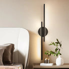 Modern black wall sconce with vertical LED light bars, mounted on a beige wall beside a bed, enhancing bedroom decor with minimalist lighting design.