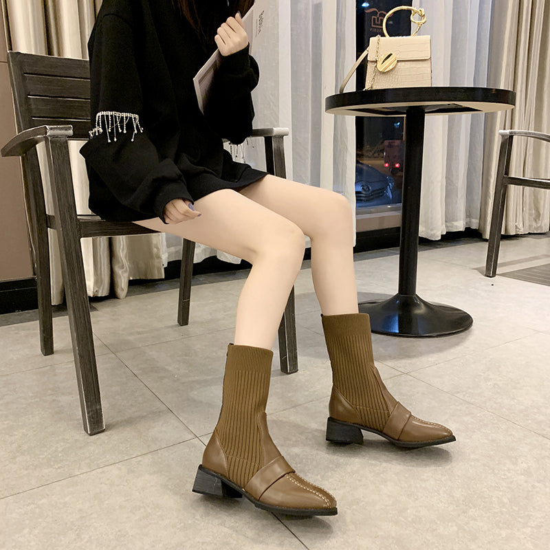 Woman wearing brown knee-high boots with block heels, sitting on a chair indoors. Fashionable outfit with a black oversized sweater.