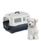 White fluffy dog sitting beside a plastic pet carrier with a black metal door, ideal for safe pet travel and transport.