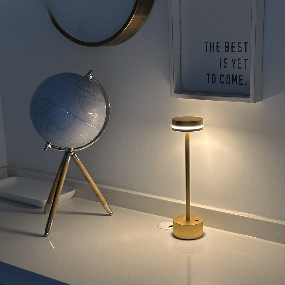 Modern gold LED table lamp on a white desk beside a decorative globe and motivational wall art, ideal for stylish home office lighting.