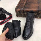 Black leather ankle boots with rugged soles, displayed in front of a vintage suitcase and a Canon camera. Stylish footwear for men.