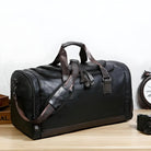 Black leather duffel bag with brown straps on a wooden table, ideal for travel or gym use. Stylish, durable, and spacious design.