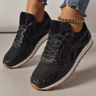 Black glitter sneakers with mesh detailing and gum soles, worn with ripped jeans and a gold anklet. Fashionable women's footwear.