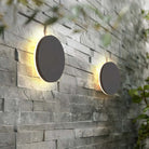 Modern round LED wall lights on textured stone wall, outdoor garden lighting, energy-efficient, minimalist design, warm glow, contemporary decor.