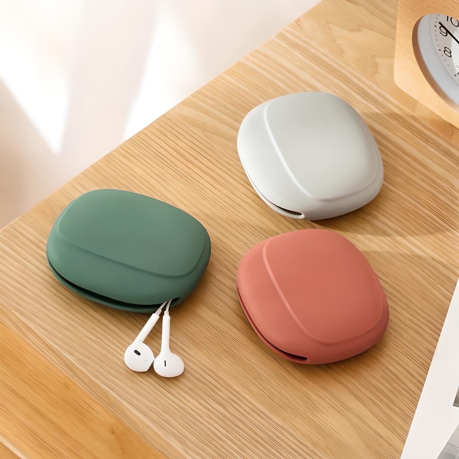 Three wireless earbud cases in green, white, and pink on a wooden table, with white earbuds nearby. Modern, minimalist design, tech accessories.