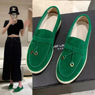 Green suede loafers with gold accents on a Saint Laurent box, paired with a stylish outfit featuring a black top, denim skirt, and bucket hat.