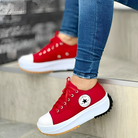 Red platform sneakers with white soles and black star logo, worn with blue jeans. Trendy casual footwear, perfect for urban fashion and street style.