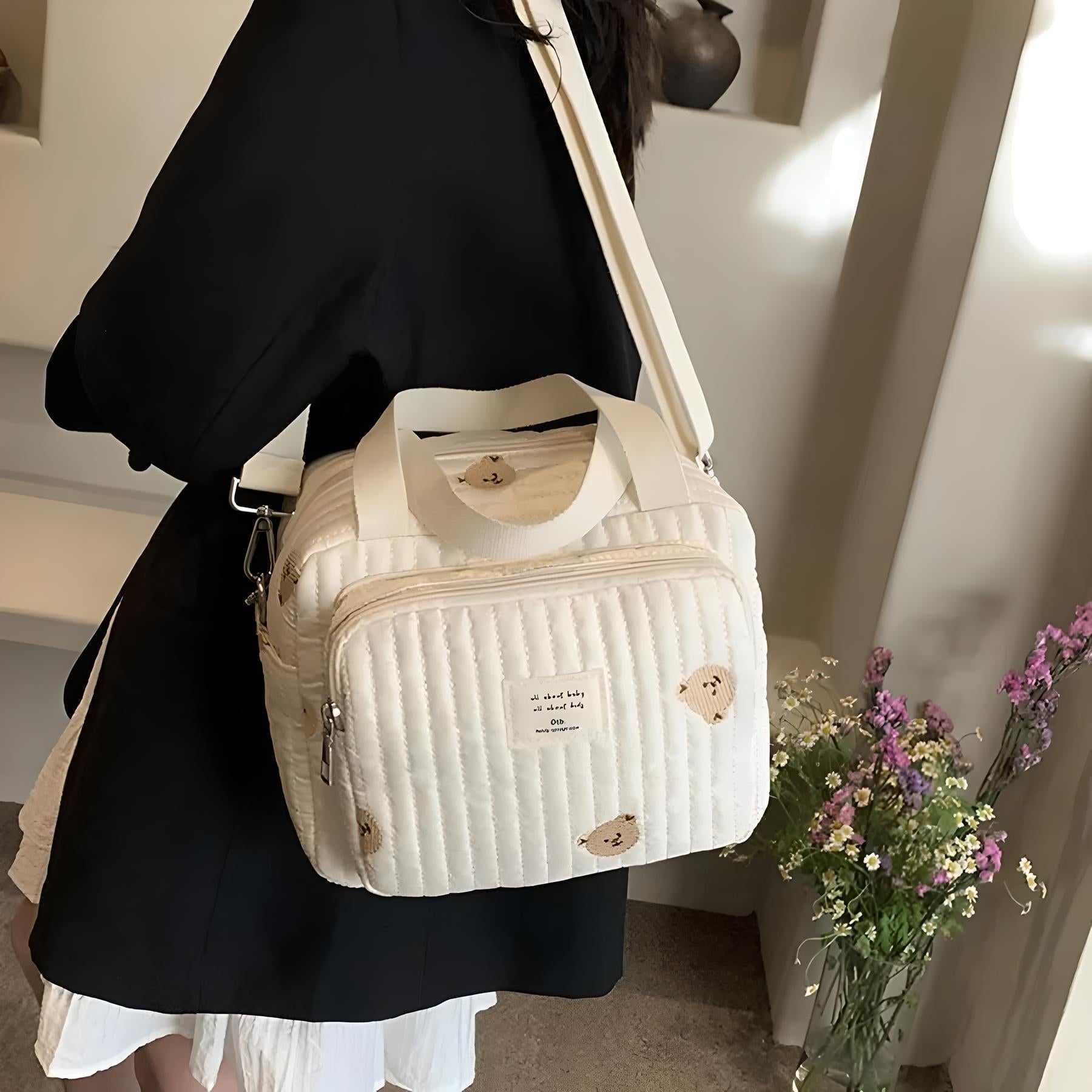 Stylish quilted white shoulder bag with bear print, worn by a person in a black coat. Perfect for casual outings. Trendy fashion accessory.