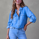 Woman wearing a stylish blue denim shirt with rolled-up sleeves and light wash jeans, showcasing casual fashion trends.