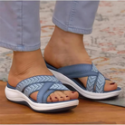 Women's blue orthopedic sandals with crisscross straps, cushioned sole, and ergonomic design for comfort and support, worn with light blue pants.