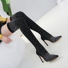 Black thigh-high stiletto boots with sparkling rhinestone embellishments, worn by a seated person. Fashionable, elegant footwear for women.