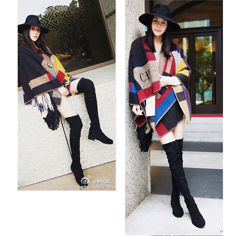 Fashionable woman wearing a colorful plaid poncho, black wide-brim hat, and thigh-high boots, posing stylishly outdoors. Trendy fall outfit.