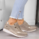 Women's metallic sneakers with perforated design and white soles, paired with light blue distressed jeans. Fashionable casual footwear.