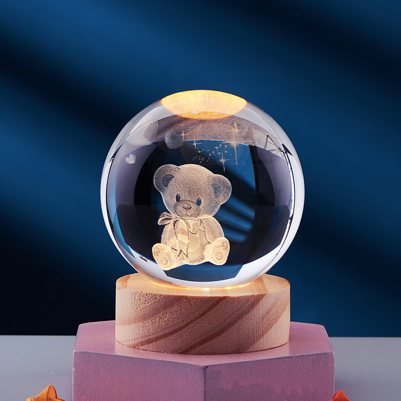 Crystal ball with 3D engraved teddy bear, illuminated on a wooden base. Perfect for home decor, gifts, or collectibles. Elegant and charming design.