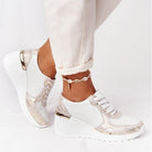 White orthopedic sneakers with gold accents, featuring a wedge heel and perforated design. Stylish and comfortable footwear for pain-free walking.