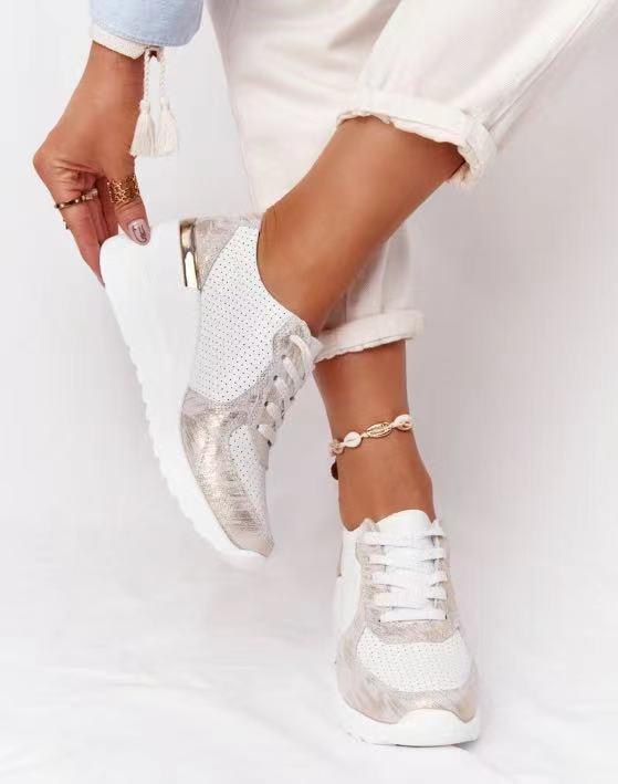 White orthopedic sneakers with metallic accents, worn by a person in rolled-up white pants, showcasing comfort and style. Perfect for pain-free walking.