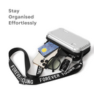 Anti-theft hardshell crossbody bag with silver finish, featuring a "Forever Young" strap, shown with smartphone, sunglasses, and car key.