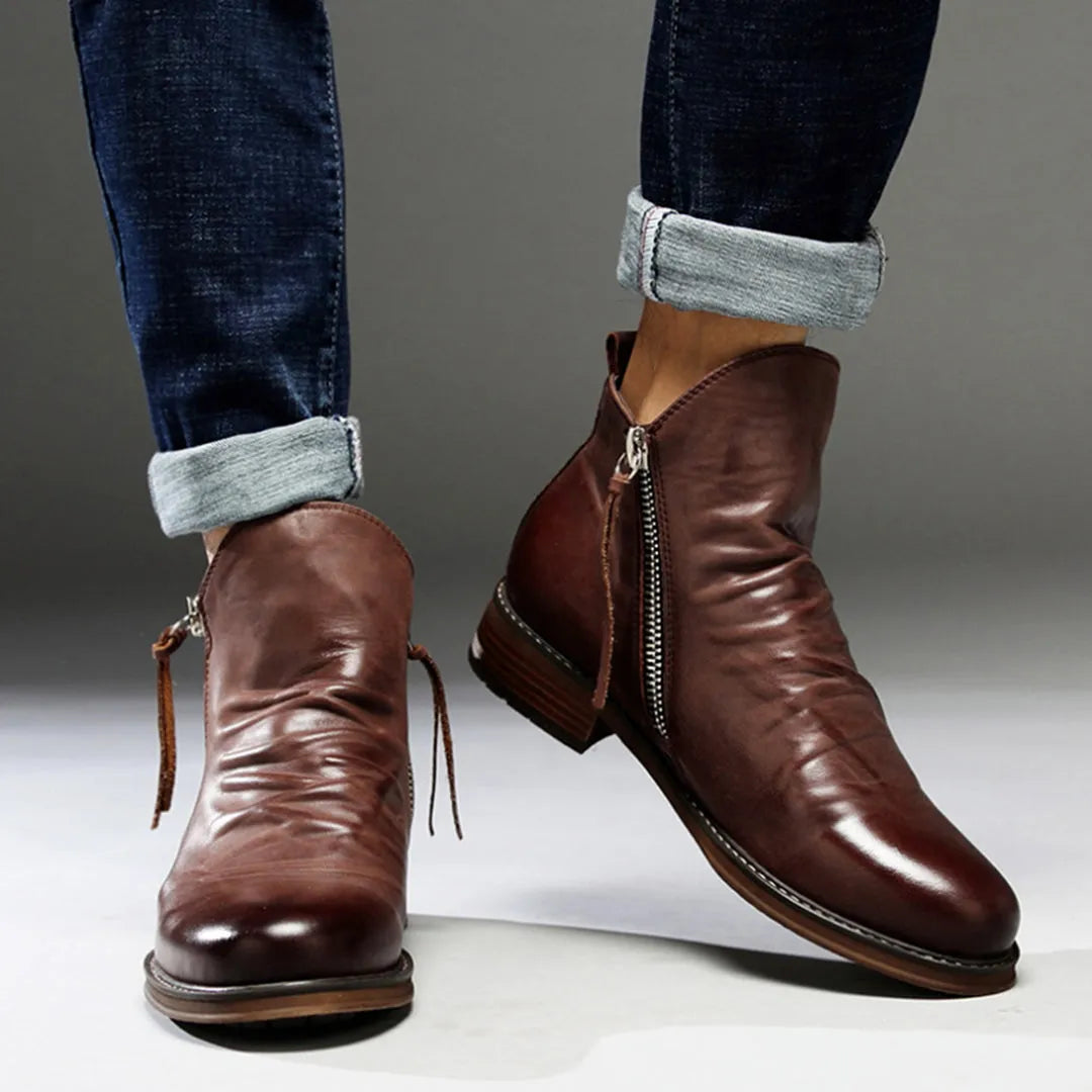 Men's brown leather ankle boots with side zippers, worn with rolled-up jeans. Stylish, casual footwear for men, perfect for fall fashion.