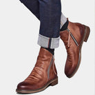 Men's brown leather ankle boots with side zippers, paired with rolled-up dark denim jeans. Stylish footwear for casual and formal occasions.