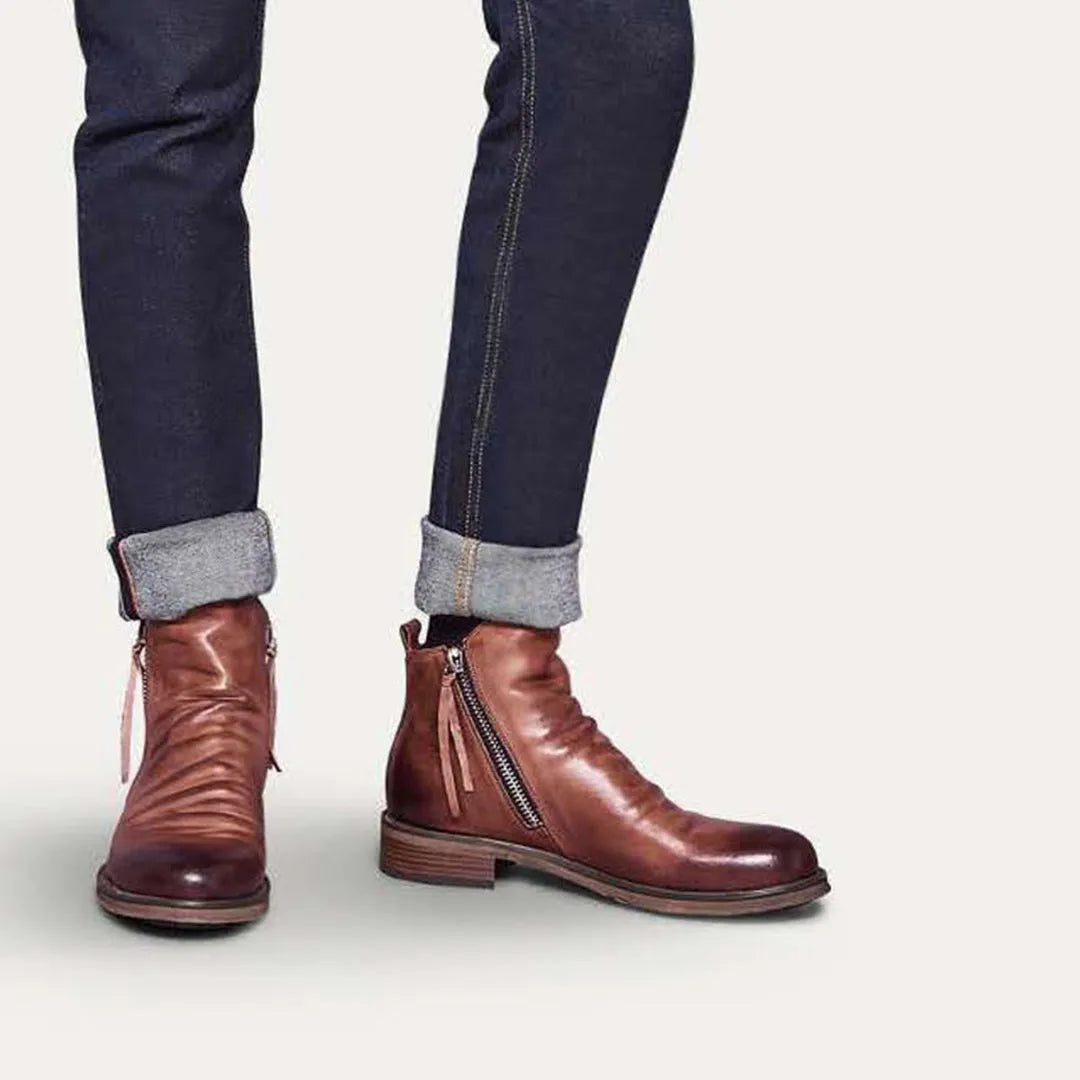 Brown leather ankle boots with side zippers, paired with dark rolled-up jeans. Stylish men's footwear, casual fashion, high-quality leather boots.