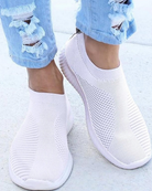 White slip-on sneakers with breathable mesh design, paired with ripped blue jeans. Stylish, comfortable footwear for casual wear. Fashionable shoes.