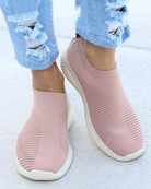 Pink slip-on sneakers with textured knit design, worn with ripped light blue jeans. Comfortable, stylish footwear for casual wear.