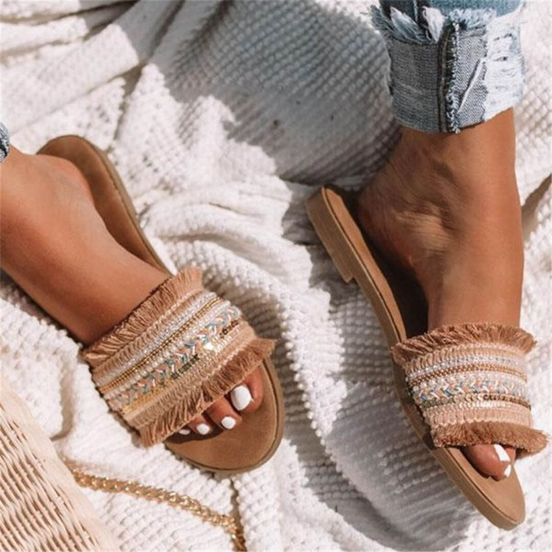 Beige fringe sandals on woman's feet, styled with distressed jeans on textured white blanket. Summer fashion footwear, boho chic style.