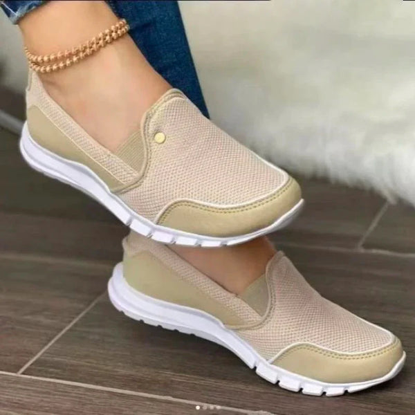 Beige slip-on sneakers with white soles, featuring breathable mesh fabric, worn with a gold anklet. Perfect for casual wear and walking comfort.