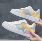 Stylish pastel sneakers with daisy flower design, featuring yellow and gray panels, white soles, and decorative chain, perfect for casual fashion.