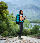 Woman hiking with trekking poles and backpack on rocky trail, surrounded by lush greenery and mountains. Outdoor adventure, nature exploration.