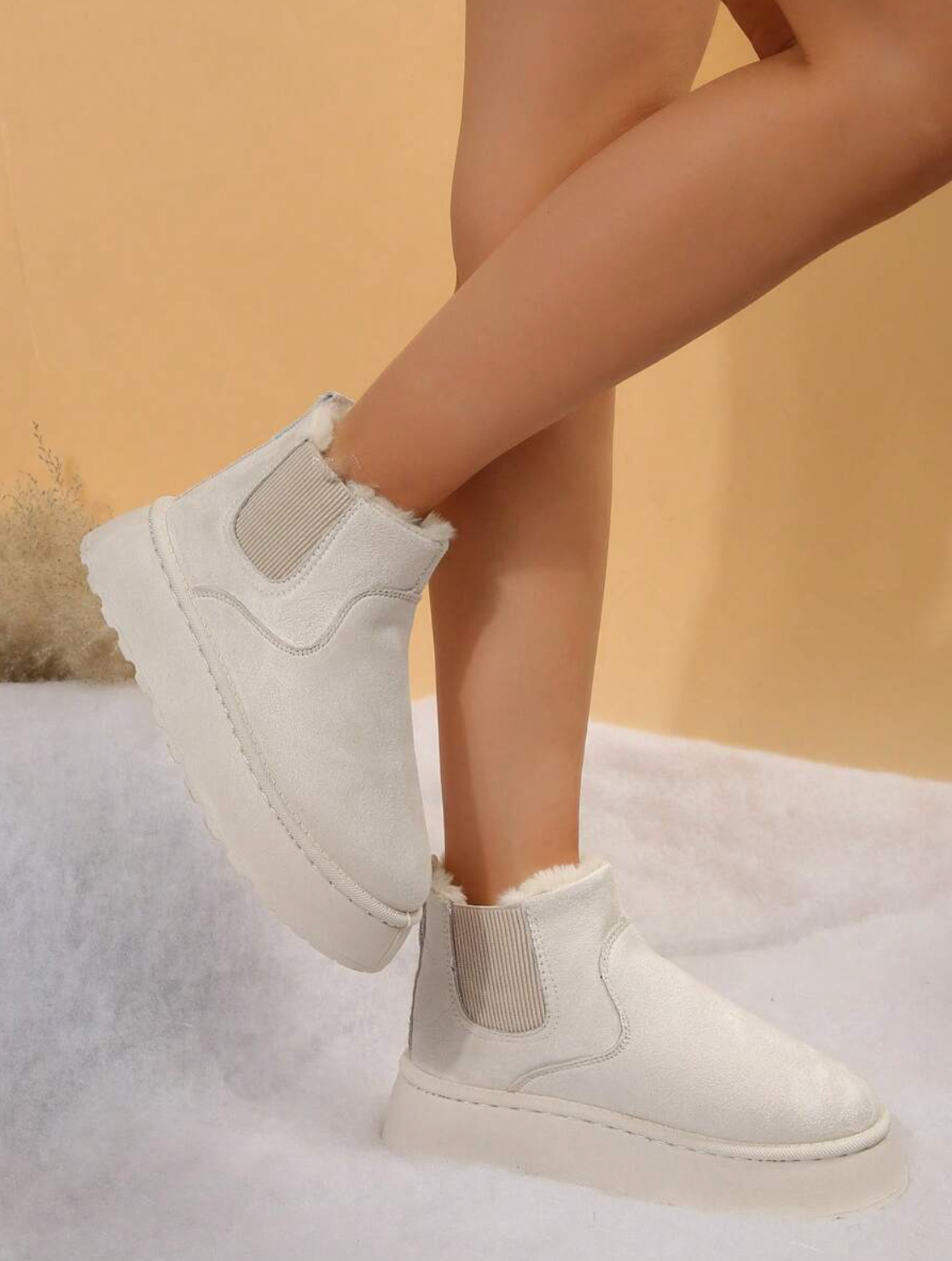 White ankle boots with fur lining on a soft surface, featuring elastic side panels and a chunky sole. Stylish winter footwear for women.