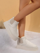 White ankle boots with fur lining on a soft surface, featuring elastic side panels and a chunky sole. Stylish winter footwear for women.