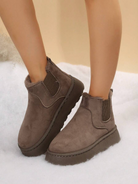 Brown suede ankle boots with faux fur lining, elastic side panels, and thick soles on a snowy background. Winter footwear, cozy fashion.