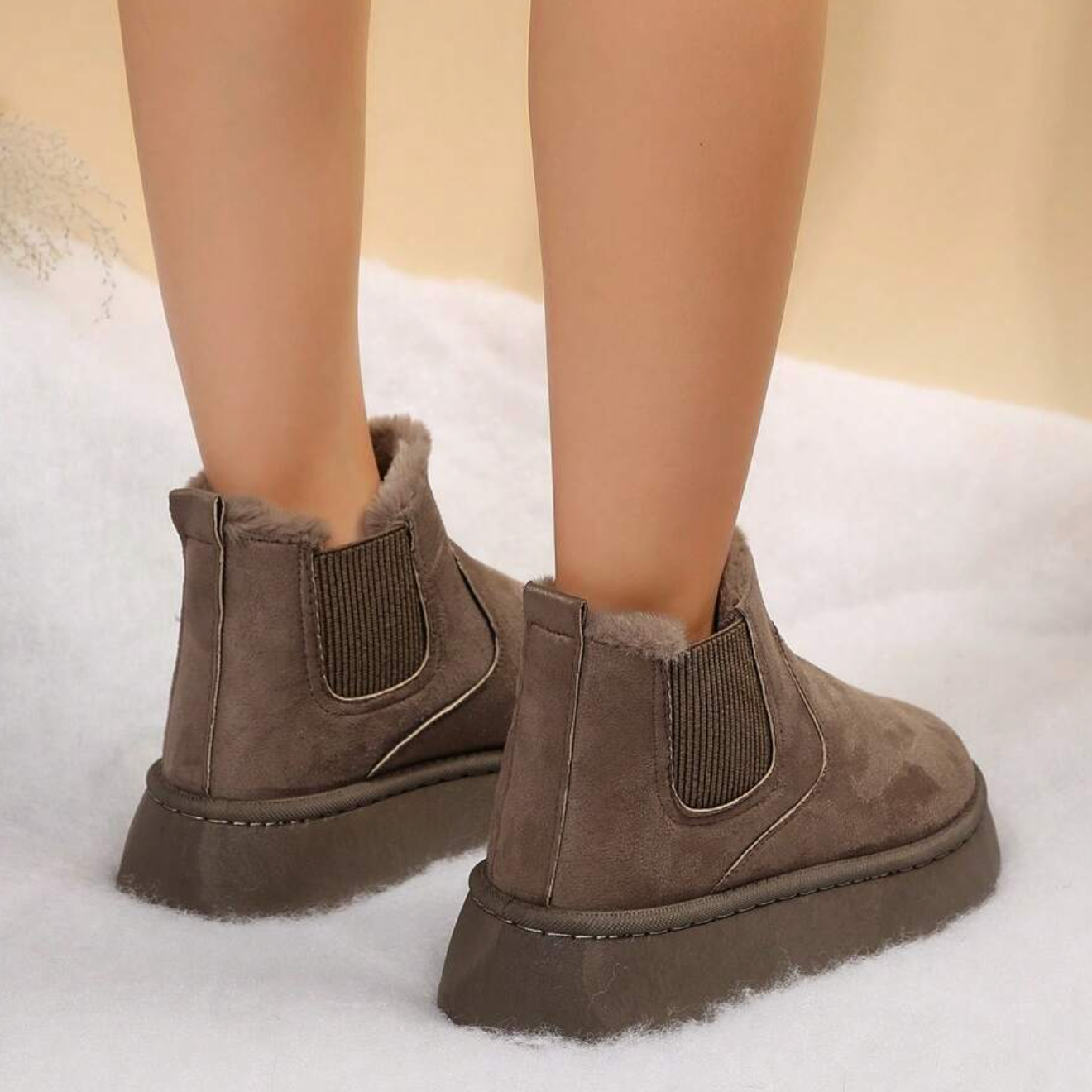 Brown suede ankle boots with faux fur lining, elastic side panels, and thick soles on a snowy background. Winter footwear fashion, cozy boots.