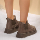 Brown suede ankle boots with faux fur lining, elastic side panels, and thick soles on a snowy background. Winter footwear fashion, cozy boots.