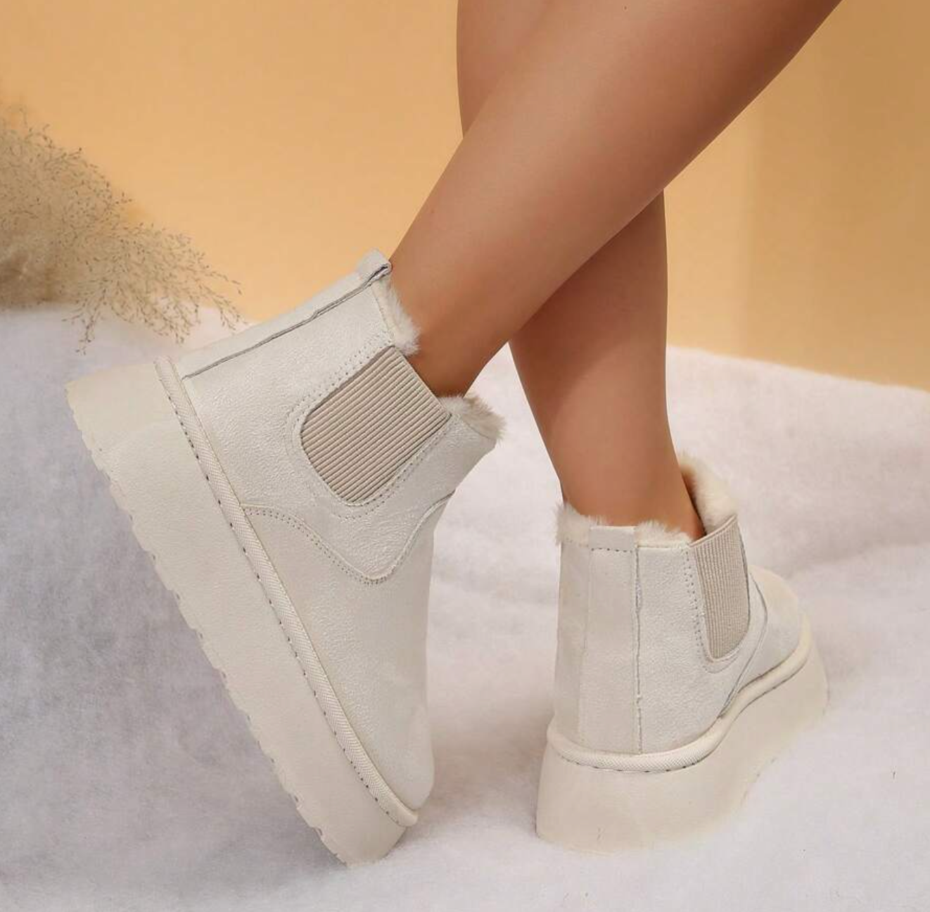 White faux fur ankle boots with platform sole, worn by a model on a soft, textured surface. Stylish winter footwear, cozy and trendy design.