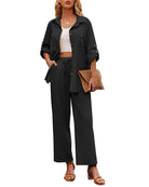 Woman in stylish black two-piece outfit with button-up shirt and wide-leg pants, holding a woven clutch. Fashionable casual wear for women.