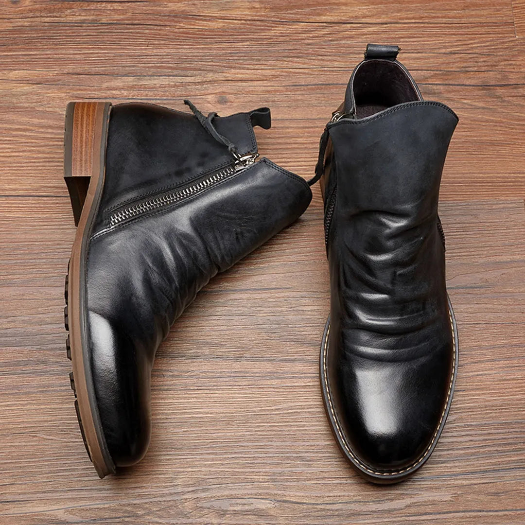 Black leather ankle boots with side zippers on a wooden floor; stylish men's footwear, durable sole, perfect for casual and formal wear.