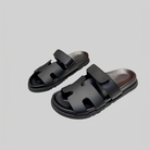 Black leather sandals with adjustable straps on a gray background, featuring a modern design and comfortable sole. Perfect for casual wear.