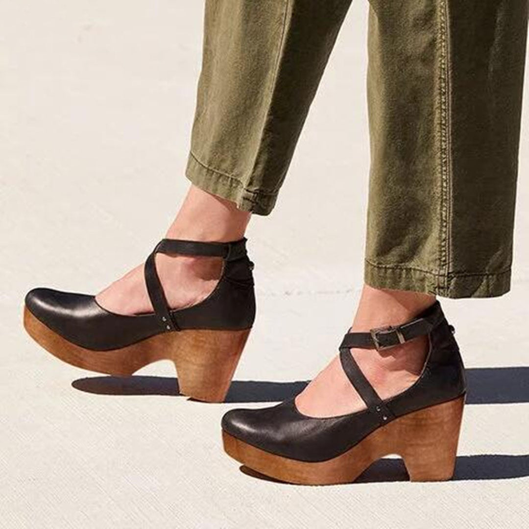 Women's black leather wedge heels with ankle straps, featuring wooden platform soles. Stylish footwear for casual and formal occasions.