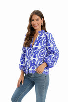 Woman wearing a blue and white patterned blouse with floral design, paired with blue jeans. Fashionable casual outfit, long sleeves, smiling model.