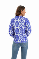 Woman wearing a blue and white floral embroidered blouse with long sleeves, paired with light blue jeans. Fashionable casual outfit.