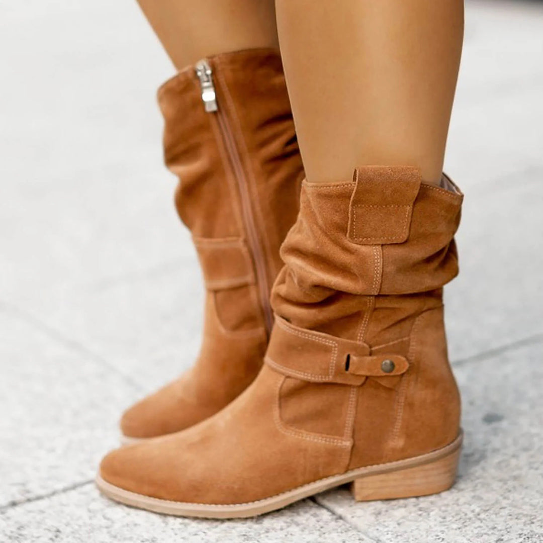 Brown suede ankle boots with side zipper and buckle detail, worn on pavement. Stylish women's fall footwear, casual fashion boots.