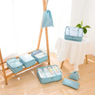 Light blue travel packing cubes set with transparent mesh tops, organized on a wooden rack and table, ideal for efficient luggage organization.