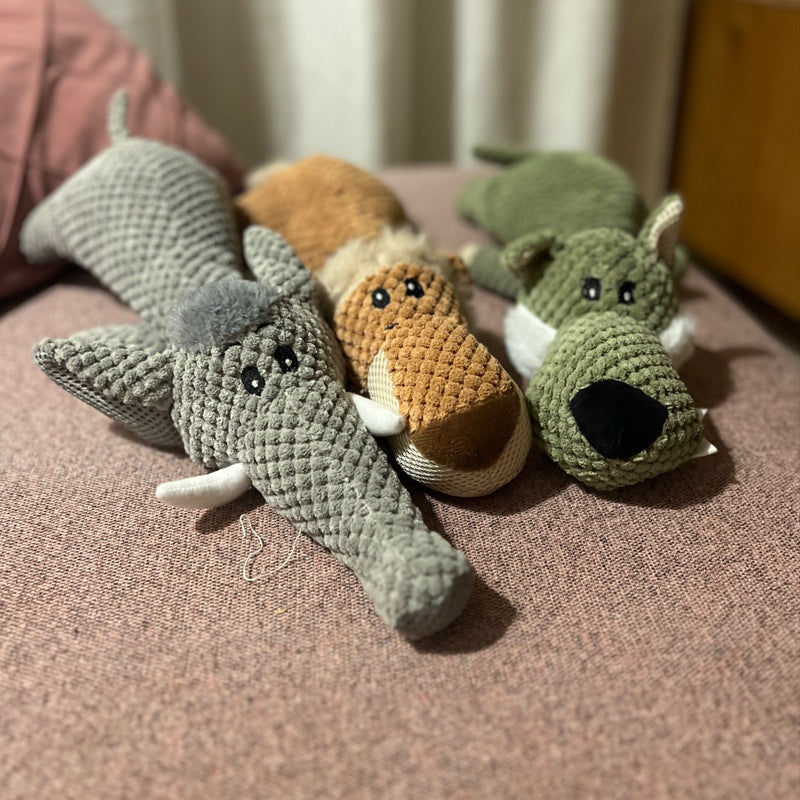 Plush dog toys on a couch, featuring a gray elephant, brown fox, and green crocodile. Interactive, durable, and perfect for pet playtime.