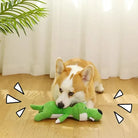 Corgi playing with green interactive dog toy on wooden floor, sunlight streaming through window, enhancing playful pet scene.