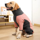 Dog wearing a pink and gray fleece jacket, sitting indoors on wooden floor. Cozy pet clothing, stylish dog apparel, warm fleece jacket for dogs.